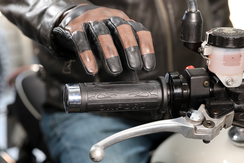 Nahaufnahme von vorn: Eine behandschuhte Hand greift nach einem Heizgriff an einem Motorradlenker.