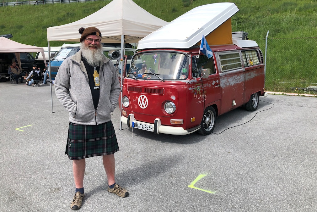 Mann im Schottenrock vor rotem VW T2 Camper