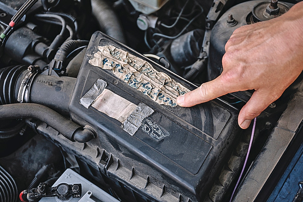 Ein Finger zeigt auf einen verschrumpelten Aufkleber im Motorraum des Volvo 850