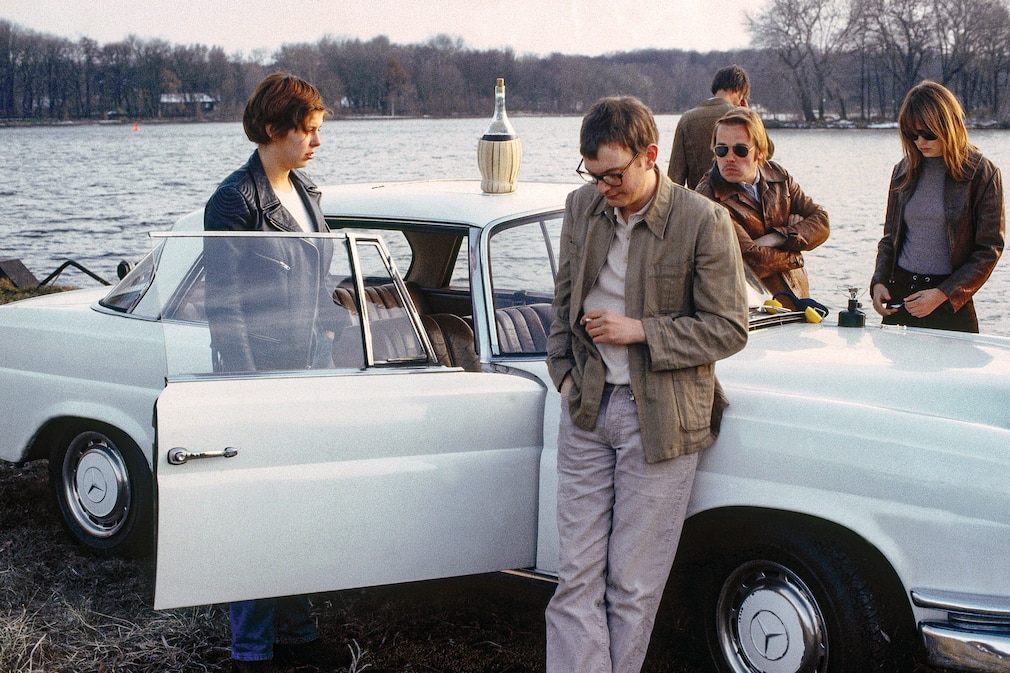 Filmszene mit vier Personen an einem weißen Mercedes W 111 Coupé