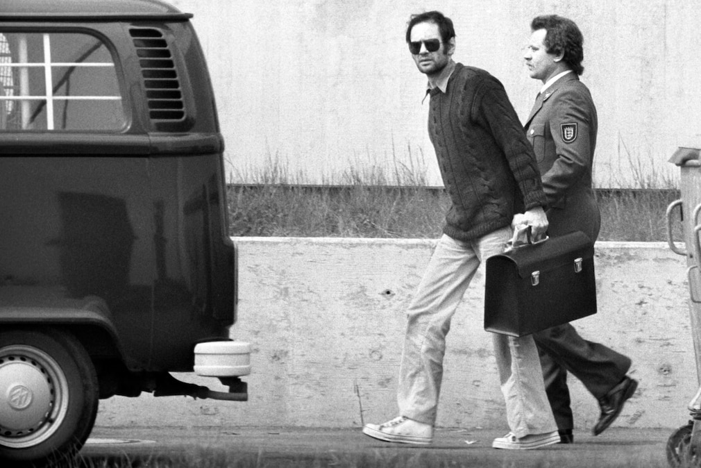 Schwarzweißfoto, Baader wird von einem Uniformierten in Richtung eines VW T2 geführt