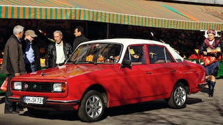 Anadol A2 in Rot von schräg vorn vor einem türkischen Laden in Deutschland, daneben ein Mann in türkischer Tracht