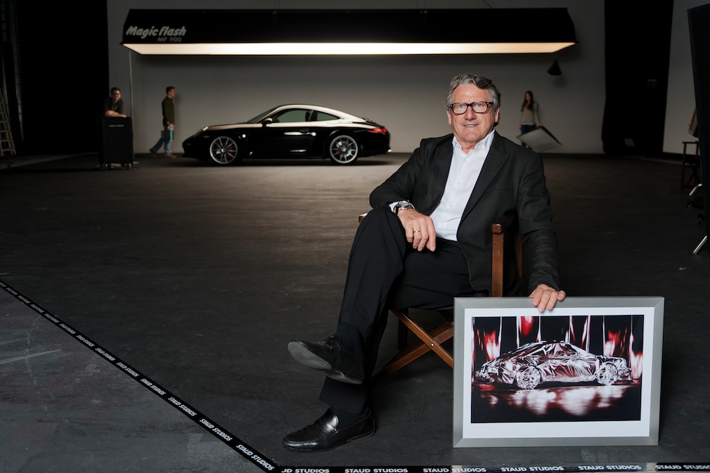 René Staud in seinem Studio, er hält ein gerahmtes Foto vom verhüllten Porsche 911 mit dem rötlichen Licht, wie er es veröffentlicht hat.