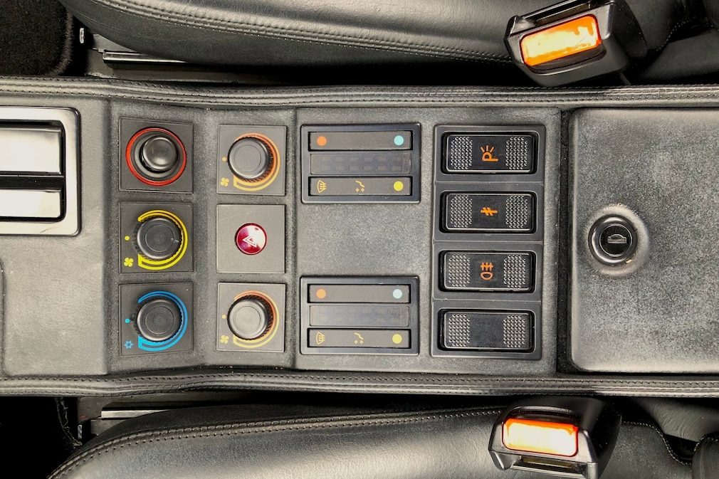 Mittelkonsole des Ferrari 328 GTS mit Klimabedienung, Zigarettenanzünder, Warnblinker, Nebel- und Parkleuchten und abschließbarem Fach. Schwarze Lederpolster.