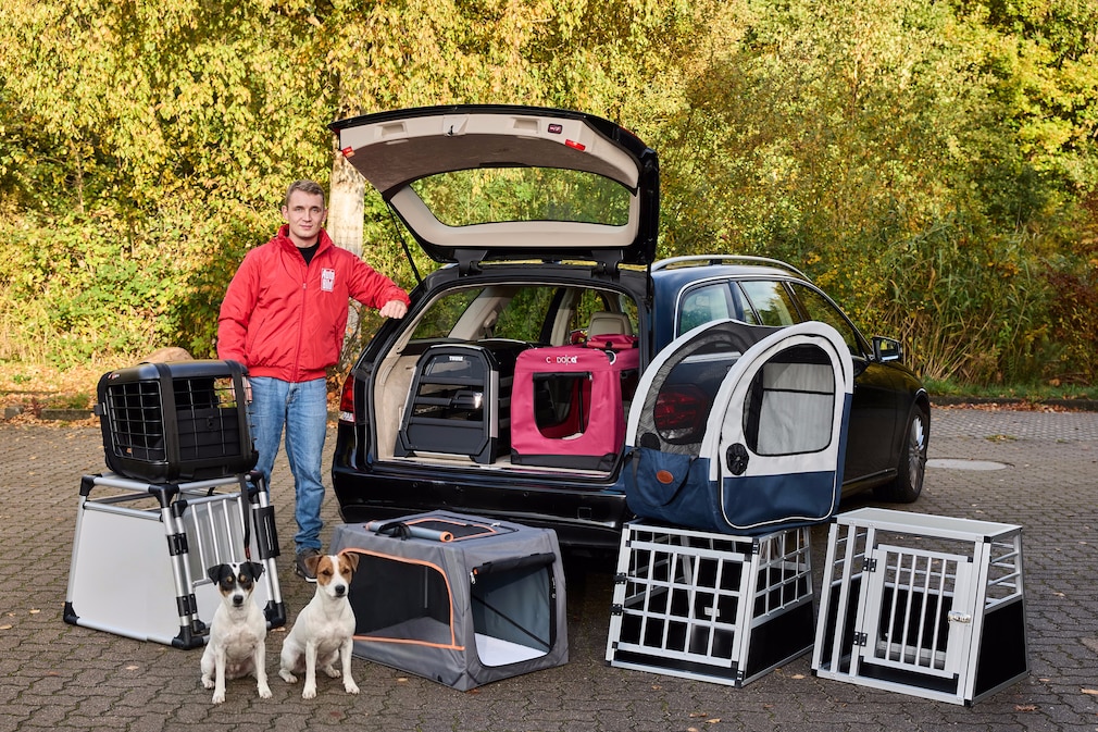 Eine Person steht an der geöffnetetn Heckklappe eines Kombis. Im Fahrzeug stehen zwei Hundeboxen, weitere stehen vor dem Fahrzeug verteilt auf einer Hoffläche.