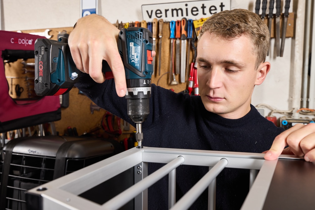 Werksattsituation: eine Person schraubt Hundeboxen mit Akkuschrauber zusammen.