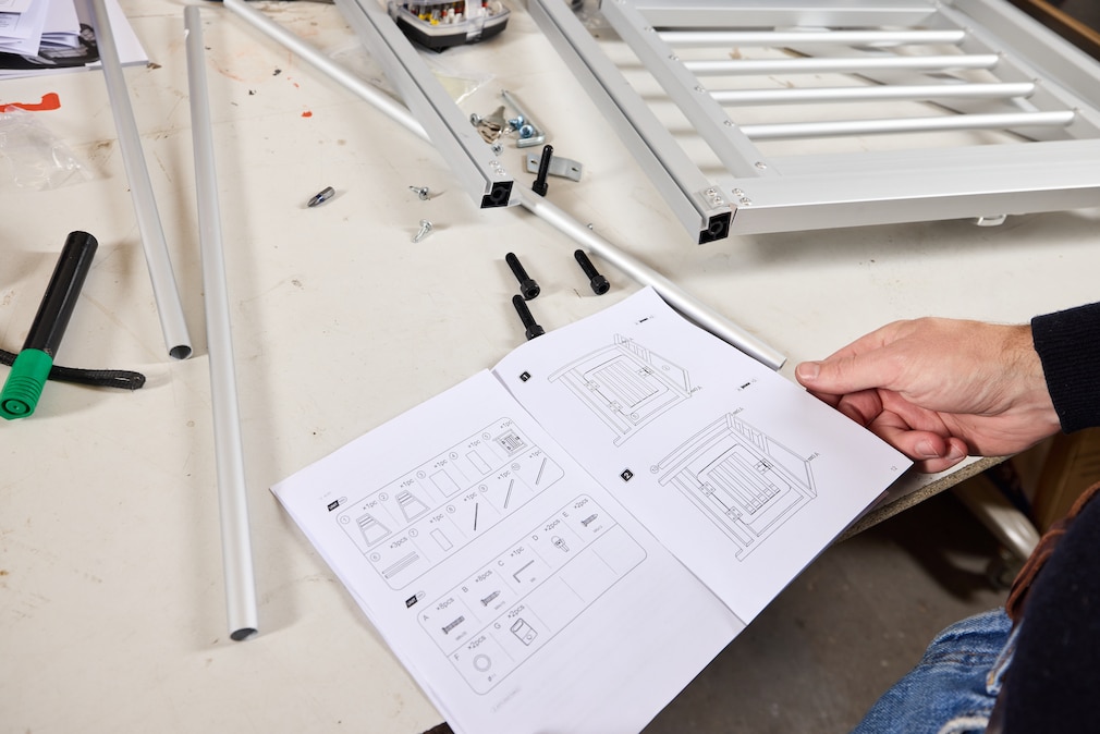 Werkstattsituation: Hundeboxen im Aufbau, zwischen den Teilen studiert eine Person die Anleitung.