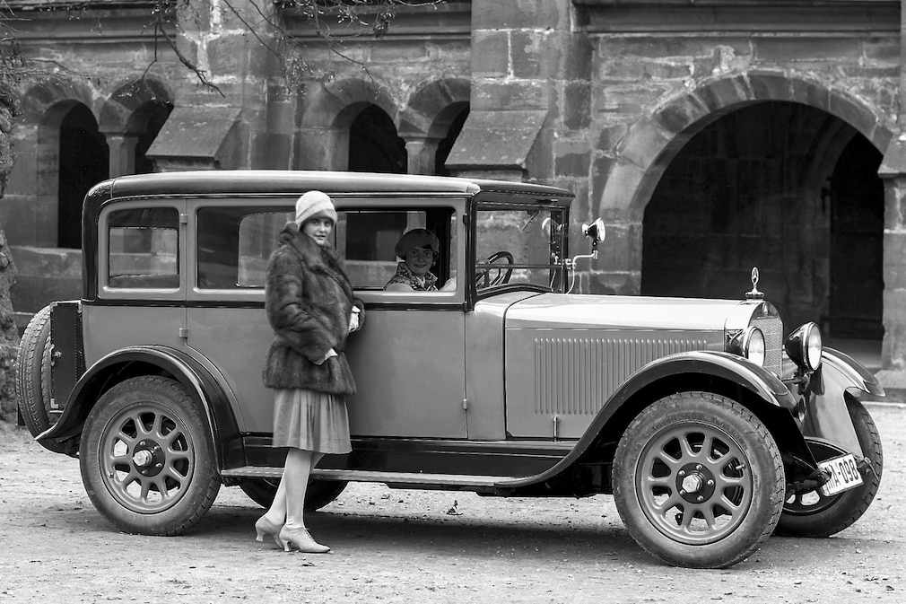 historisches Schwarzweißfoto: Mercedes 8/38 PS Typ Stuttgart 200 stehend von der Seite, eine Frau steht außen, eine sitzt am Lenkrad