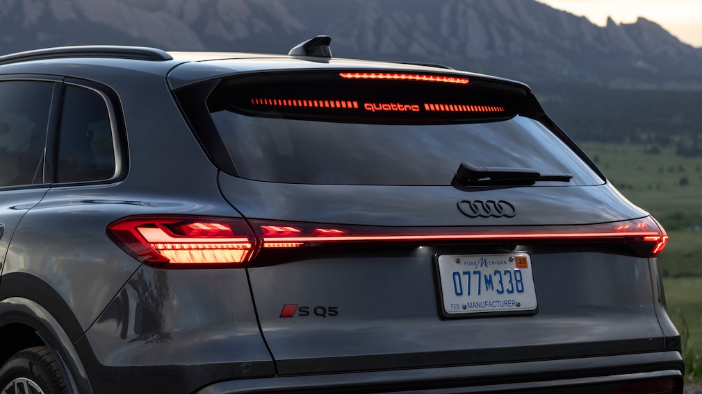 Heckansicht eines Audi SQ5 mit leuchtendem quattro-Schriftzug bei Sonnenuntergang.
