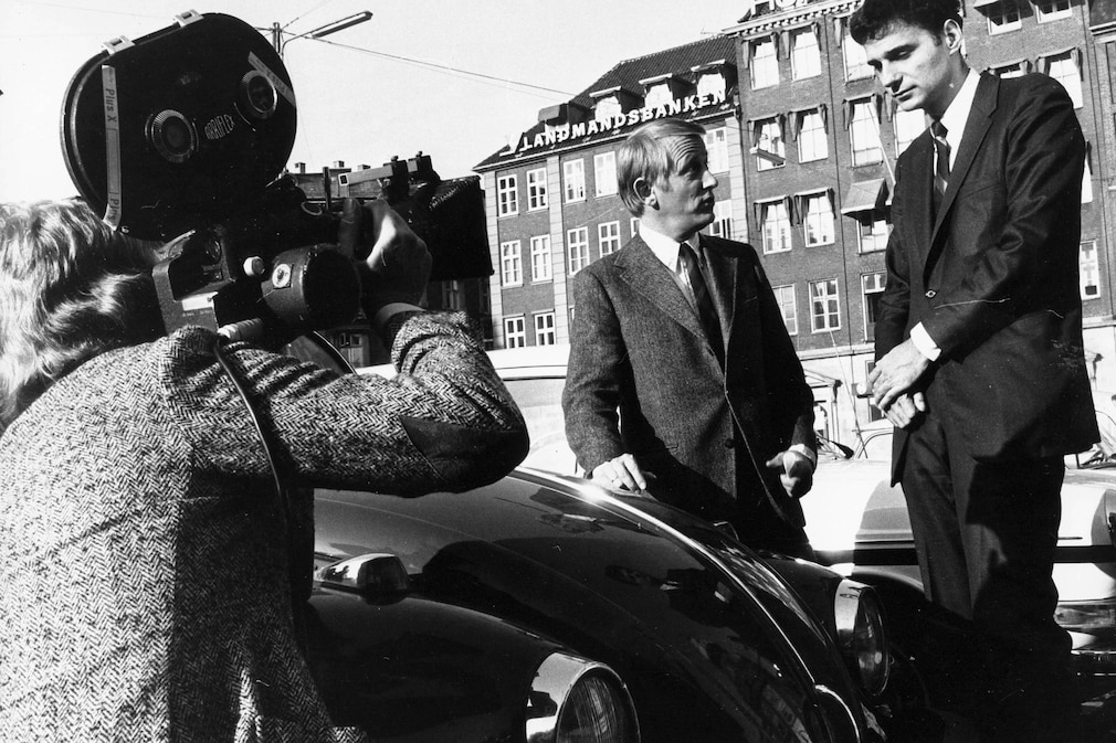 historisches Schwarzweißfoto, Ralph Nader an einem VW Käfer vor einer Fernsehkamera