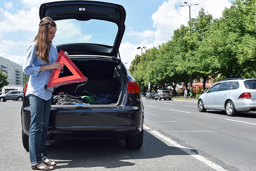 Eine junge Frau stellt am 20.06.2014 bei einer Panne das Warndreieck hinter ihrem Auto auf.