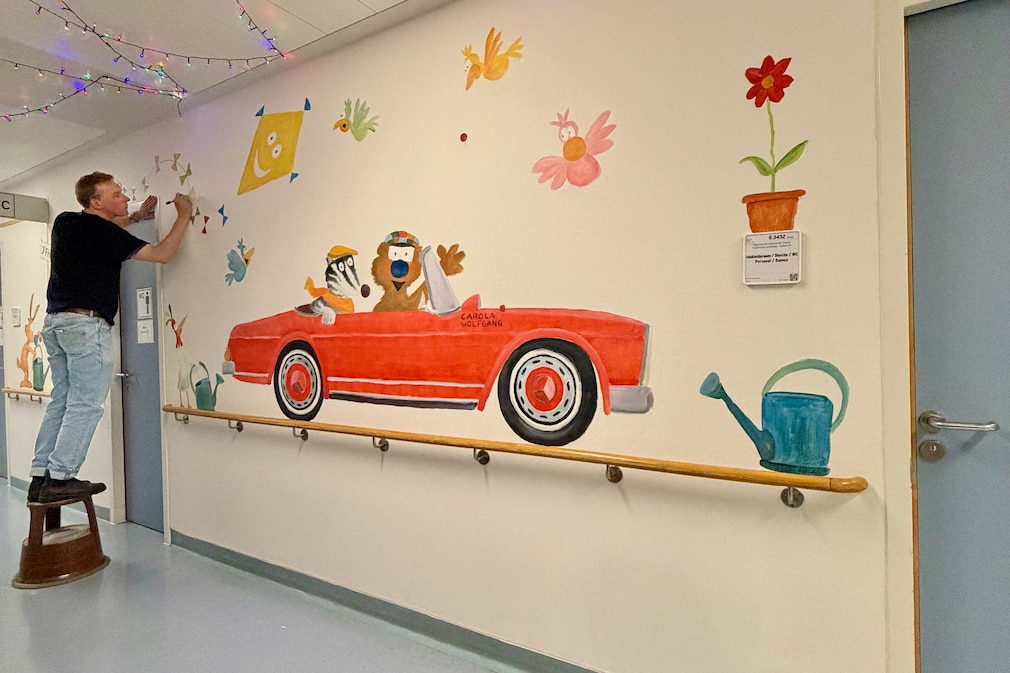 Künstler bemalt eine Flurwand in Krankenhaus. Ein Motiv ist ein Oldtimer.