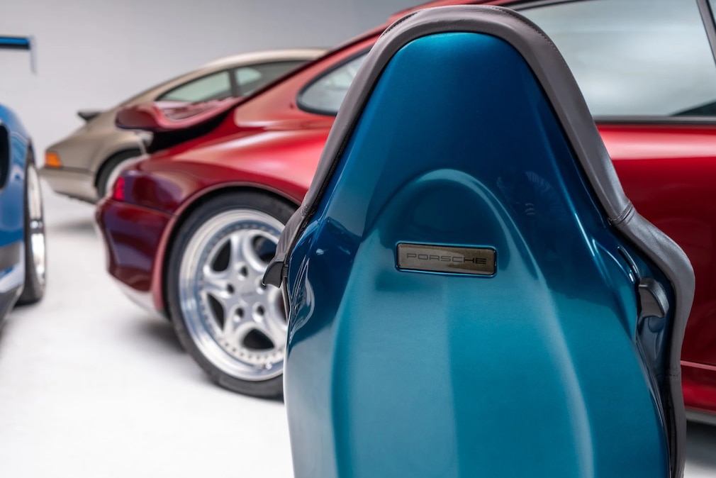 Porsche-Logo an der Rückseite des Sitzes; im Hintergrund drei Autos von Porsche