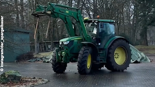 John Deere-Traktor beim Driften auf einem gepflasterten Hof.