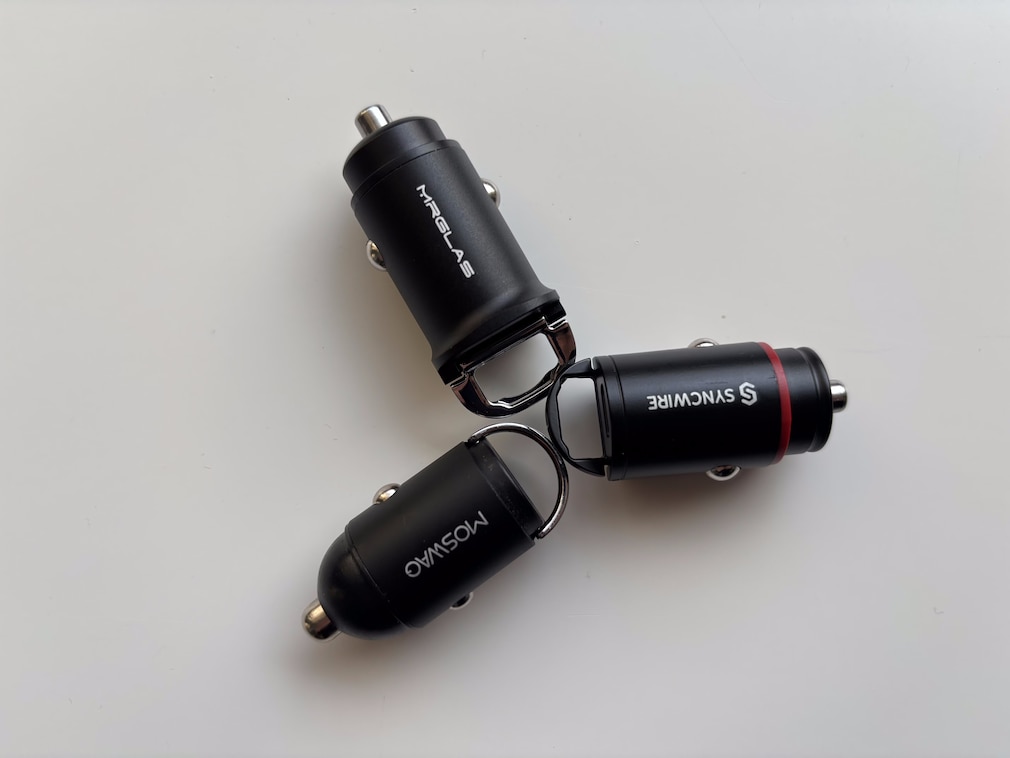 Drei 12V-USB-Adapter auf weißem Hintergrund, kompakte Modelle mit Klapp-Bügel.