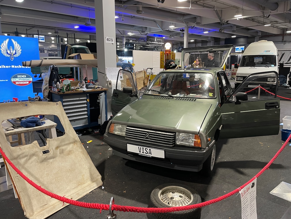 Auf einem Messestand, der mit rotem Band abgesperrt ist, steht ein grüßer Citroen Visa, an dem gearbeitet wird.