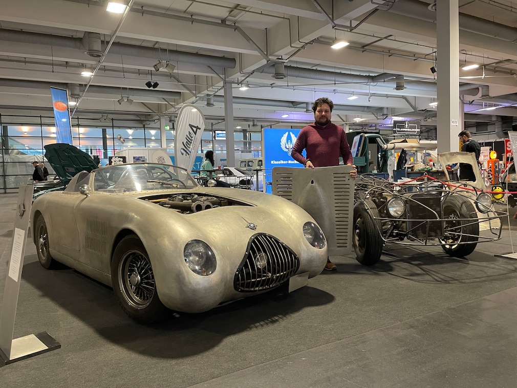 Mann steht zwischen zwei Eigenbau-Karosserien auf Vorkriegschassis und hält eine selbstgebaute Motorhaube in der Hand.
