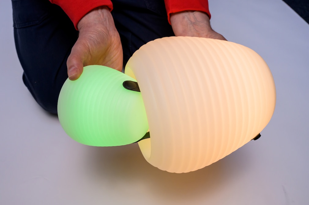 Ausschnitt einer Person, die in beiden Händen jeweils eine Lampe hält und die kleiner Lampe in die Öffnung im Boden der größeren schiebt