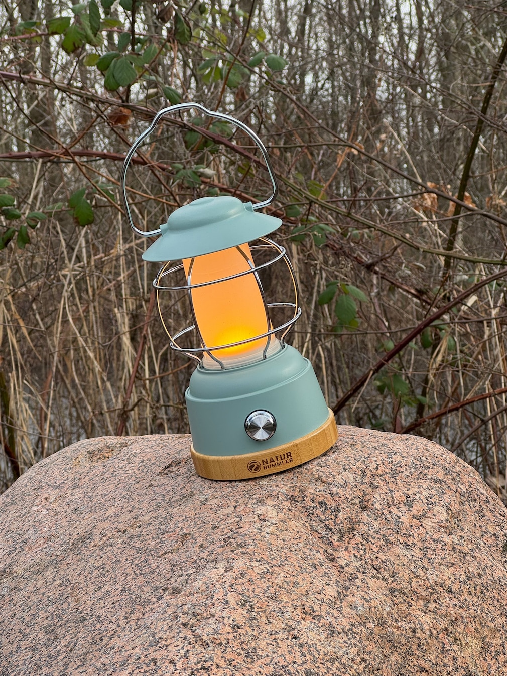 LED-Laterne steht mit eingeschaltetem (warmen) Licht auf einem großen Stein in der Natur.