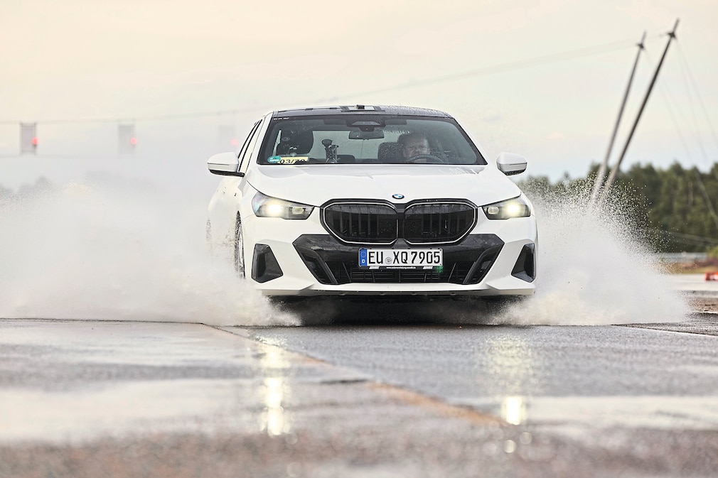 Wasserfontänen spritzen aus den Radhäusern des Testfahrzeugs, während es über die Aquaplaning-Versuchsstrecke fährt.