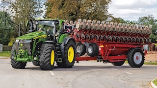 John Deere 8R Traktor mit breitem Anbaugerät im Straßenverkehr