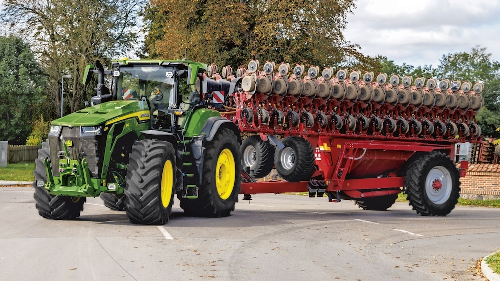 John Deere 8R Traktor mit breitem Anbaugerät im Straßenverkehr