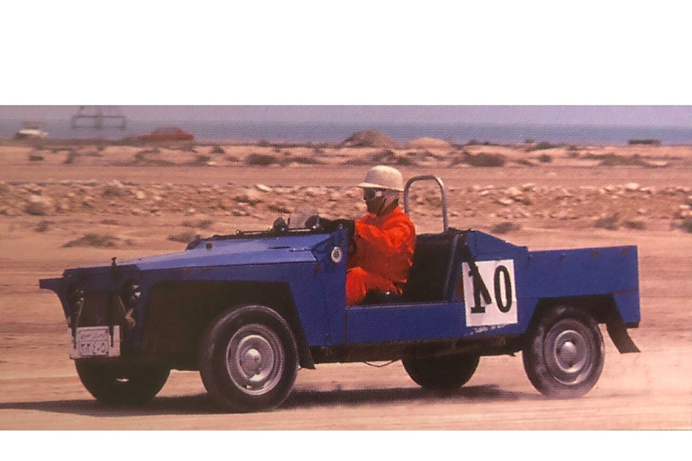 historisches Farbfoto: Saipac Jyane Mehari fahrend von der Seite, mit Startnummer und einem Fahrer mit Helm