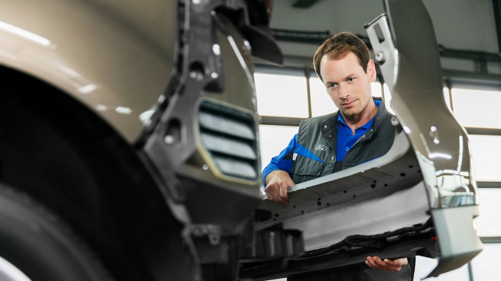 Mechaniker montiert eine Stoßstange an einem Ford-Fahrzeug in der Werkstatt.