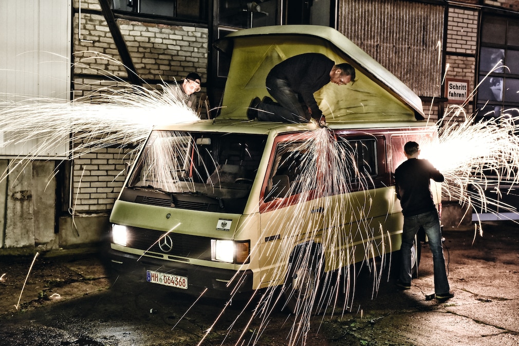 Zwei Mann arbeiten mit Winkelschleifern an einem Mercedes MB 100, Funken sprühen