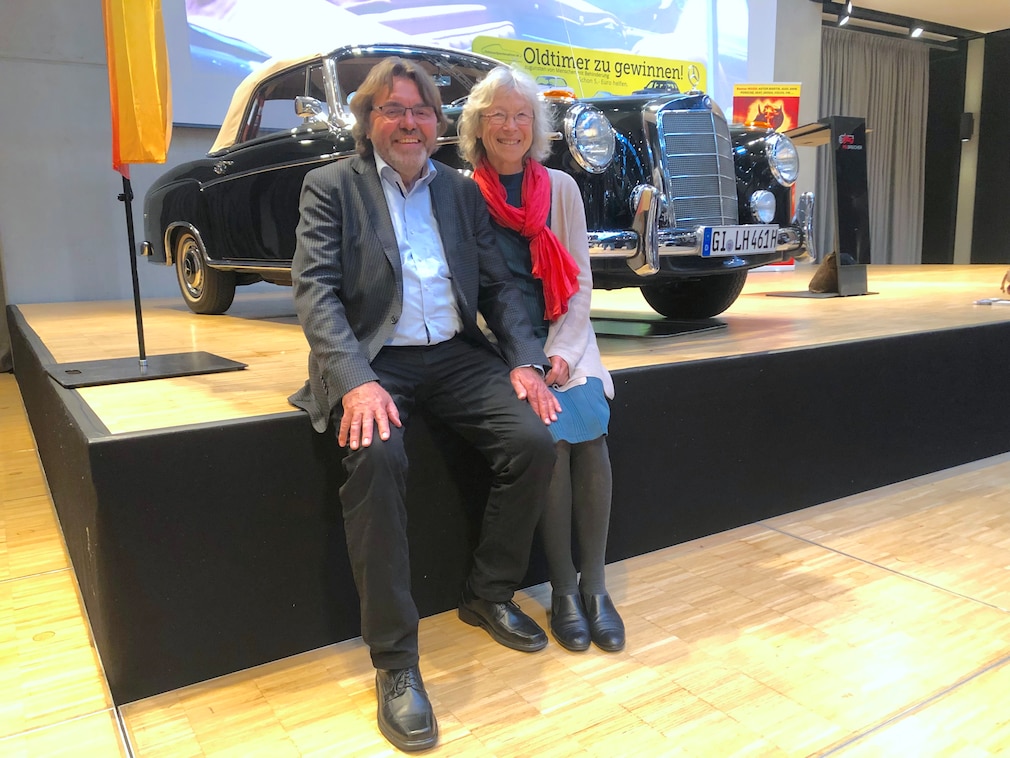 Ein Herr und eine Dame sitzen auf der Sufe einer Bühen, dahinter ihr Mercedes-Oldtimer