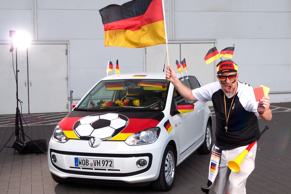 AUTO BILD-Redakteur Bendix Krohn und VW Up mit Deutschlandfahnen dekoriert