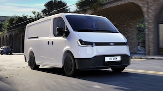 Weißer Ford Transit City Van fährt durch eine Stadtstraße mit Backsteinarkaden.