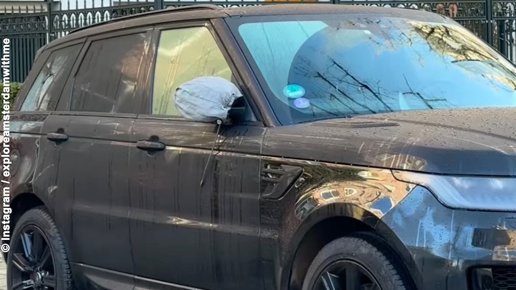 Range Rover mit Seitenspiegel in einem hellblauen Beutel parkt in einem Wohnviertel an der Straße.