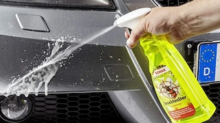 Redakteur in AUTO BILD-Jacke steht unterm Regenschirm neben einem Auto in einer laufenden Waschanlage