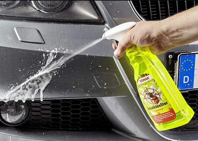 Redakteur in AUTO BILD-Jacke steht unterm Regenschirm neben einem Auto in einer laufenden Waschanlage