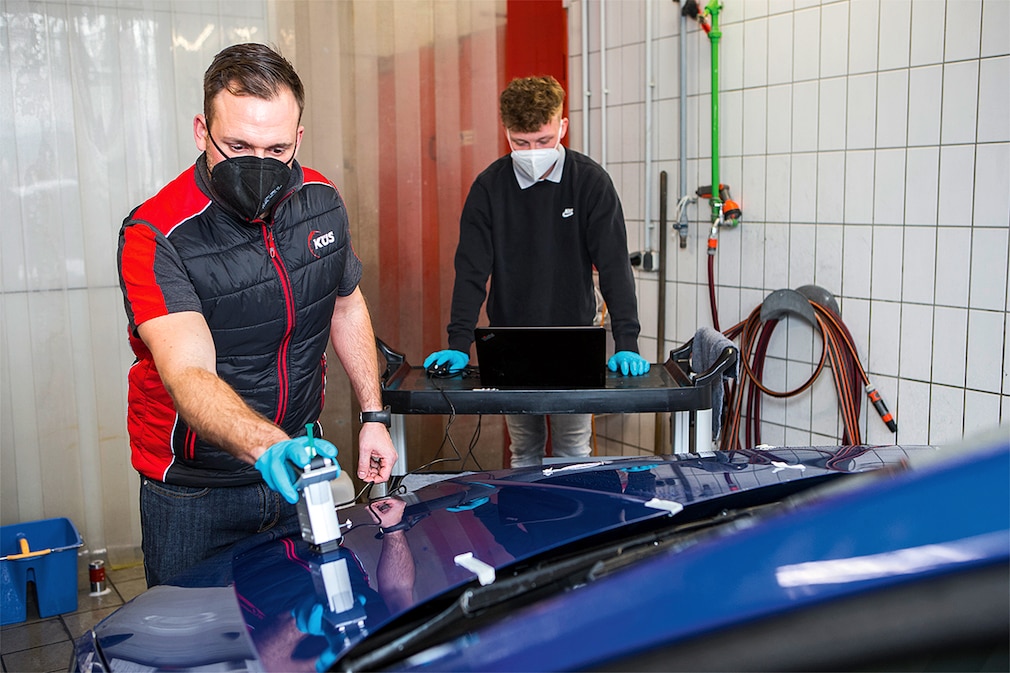 Tester prüft den Kontaktwinkel von Wassertropfen auf einer nassen, versiegelten Motorhaube.