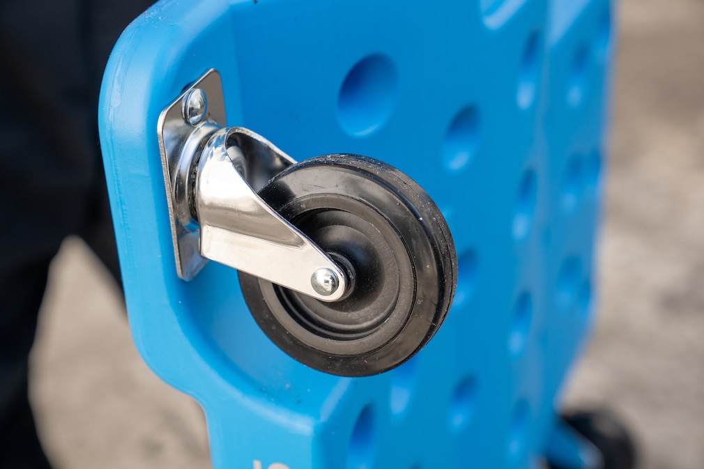 Nahaufnahme einer einzelnen Rolle eines Rollbretts: Eine gummierte Laufrolle ist an einer Metallhalterung befestigt, die an einer blauen Kunststoffschale montiert ist.