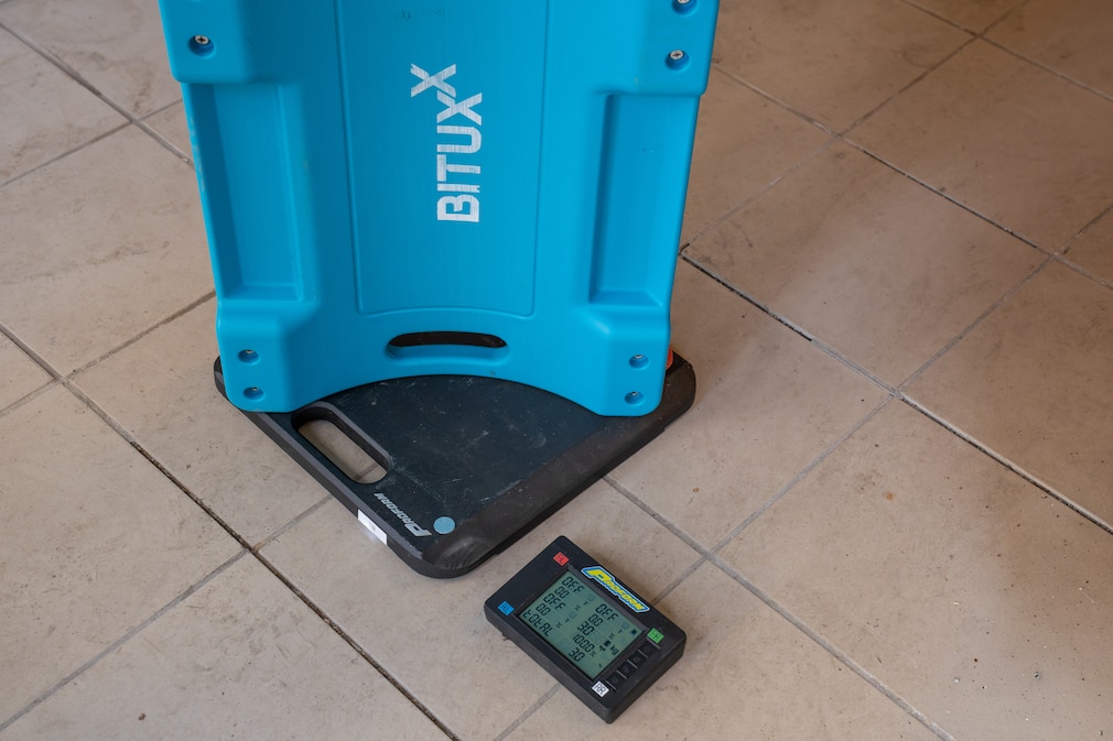 Nahaufnahme eines Rollbretts, das auf einer digitalen Waage steht. Das Display zeigt das Gewicht von 3 Kilogramm an. Im Hintergrund ist der Boden einer Werkstatt zu sehen.