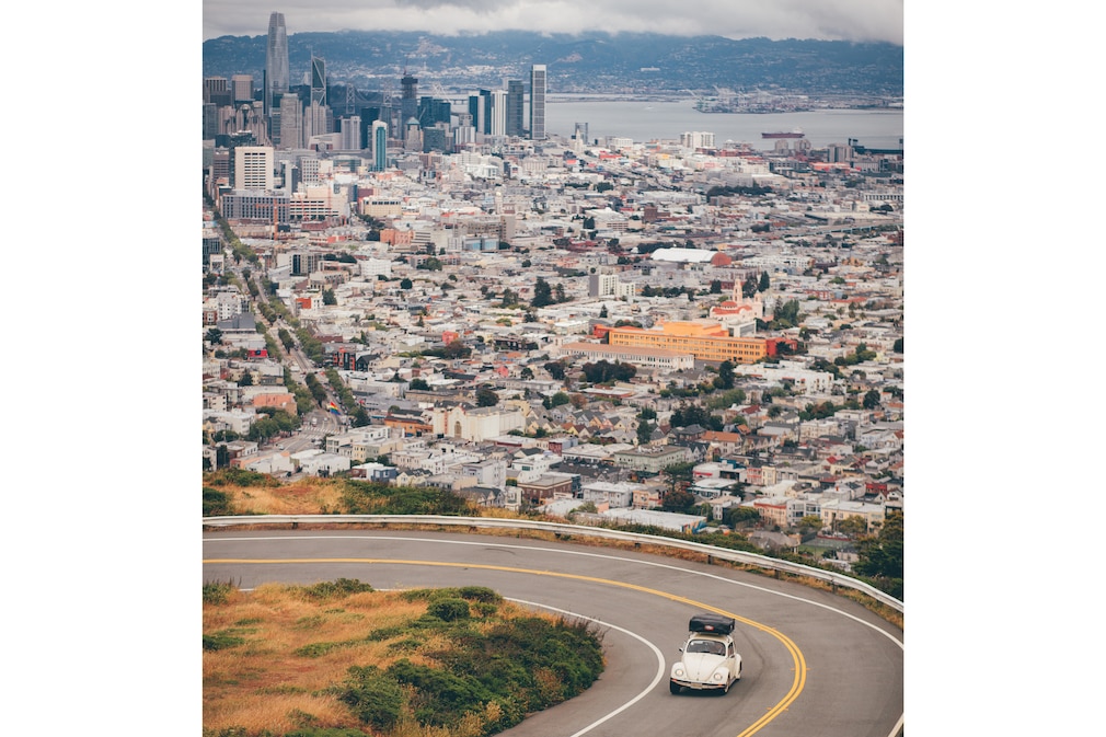 VW Käfer Última Edición mit Dachzelt fahrend schräg von oben, im Hintergrund San Francisco