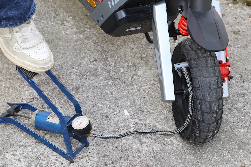Detailaufnahme einer Person, die mit einer Standluftpumpe den Reifendruck am Vorderrad eines NAVEE XT5 Max kontrolliert.