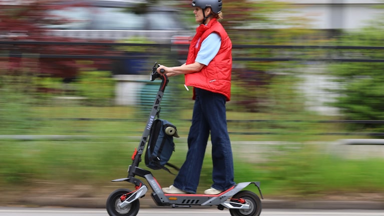 Eine Person fährt mit dem NAVEE XT5 Max auf einer Straße. Am Lenker hängt eine Sporttasche, während der Hintergrund durch die Fahrbewegung unscharf erscheint.