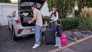 Family packing luggage for vacation with electric car in driveway