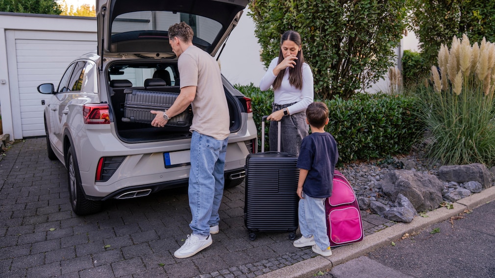 Family packing luggage for vacation with electric car in driveway