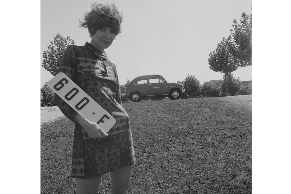 Historisches Schwarzweißfoto: Seat 600 F mit Frau in Minierock