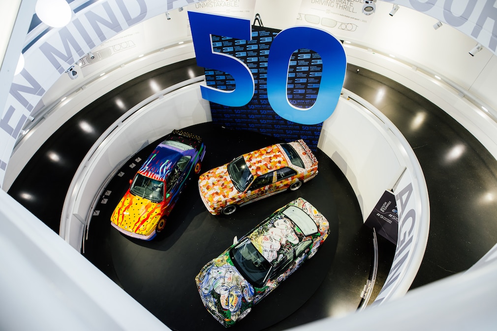 Drei BMW Art Cars von oben in einer Ausstellung, an der Wand eine große 50