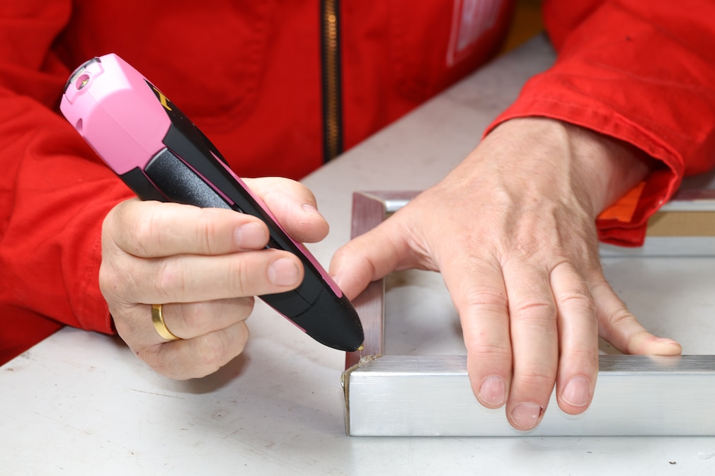 .Eine Hand hält den Steinel-Heissklebestift an einen liegenden Bilderrahmen beim Verkleben.
