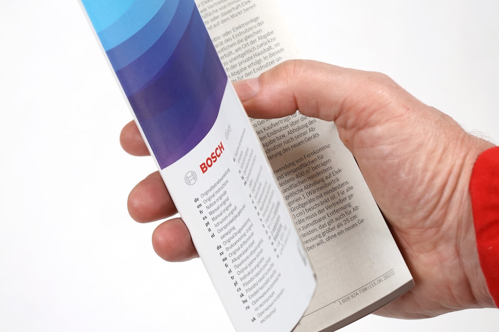 Eine Hand hält die Bosch Gluey-Bedienungsanleitung. Man kann die Angabe der unterschiedlichen Sprachen sehen.