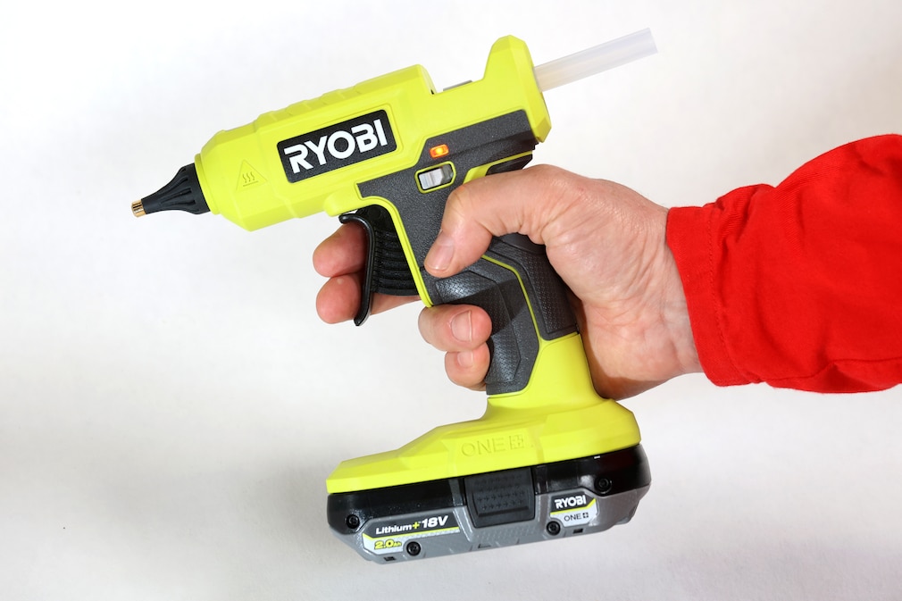 Seitenansicht: Eine Hand hält eine Akku-Heißklebepistole von Ryobi.