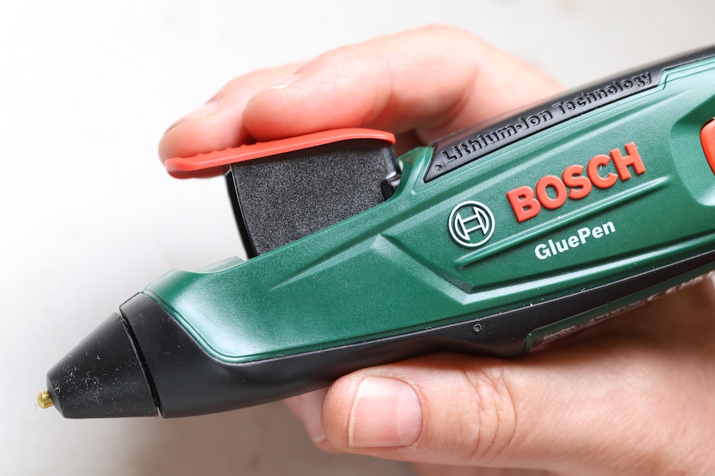 Seitenansicht: Eine Hand hält einen Akku-Heißklebestift von Bosch.