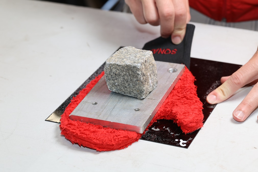Redakteur zieht mit Platte und Stein beschwerten Waschhandschuh über die Testtafel.